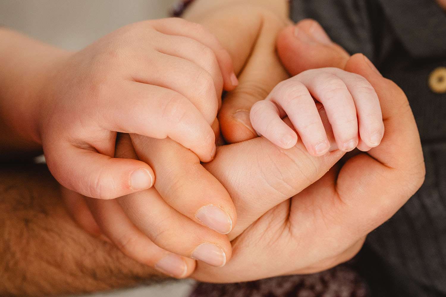 Hände von Vater, Mutter, Newborn und Kleinkind