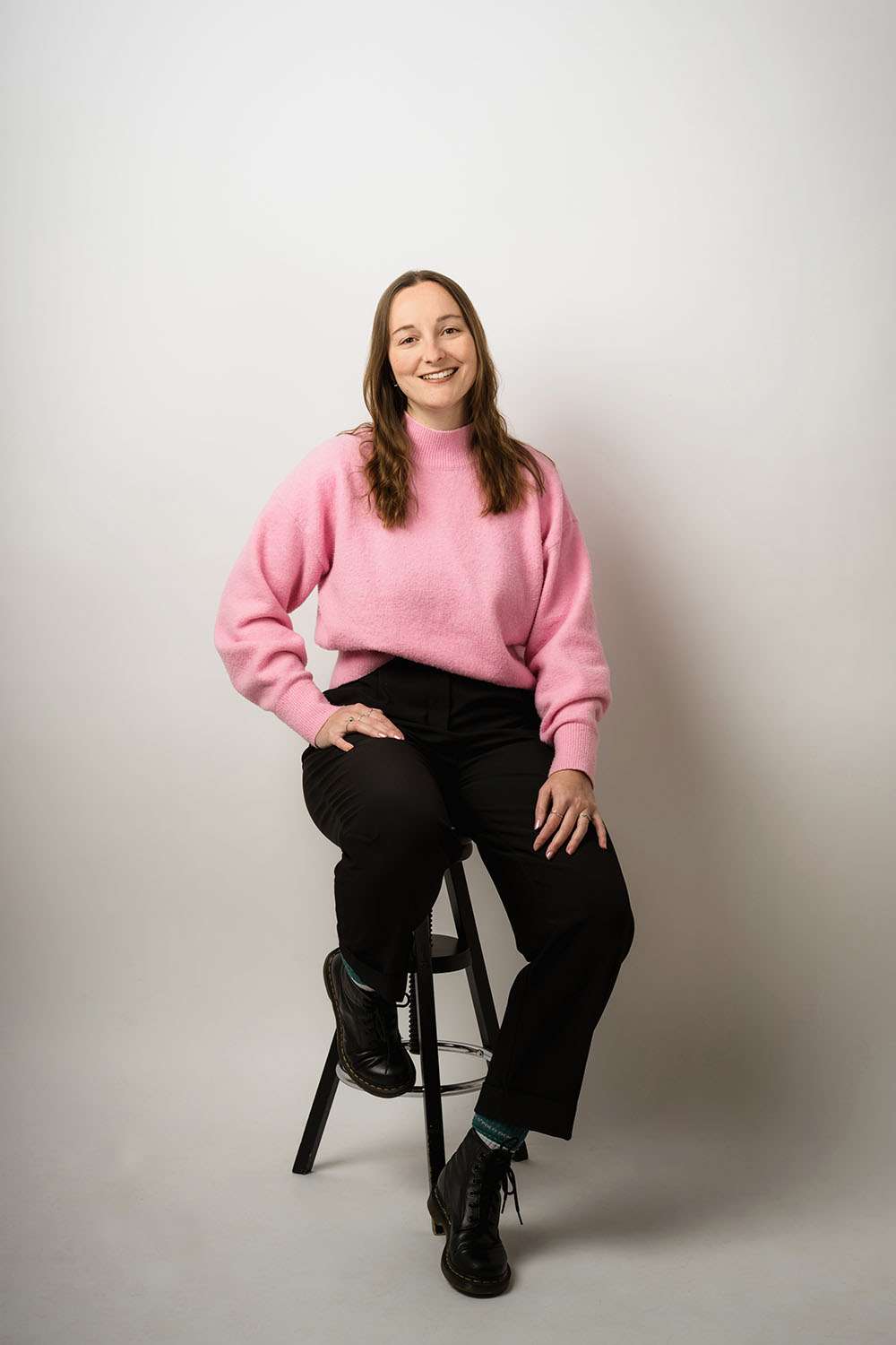 Frau mit pinken Pulli sitzt auf Hocker in einem Fotostudio
