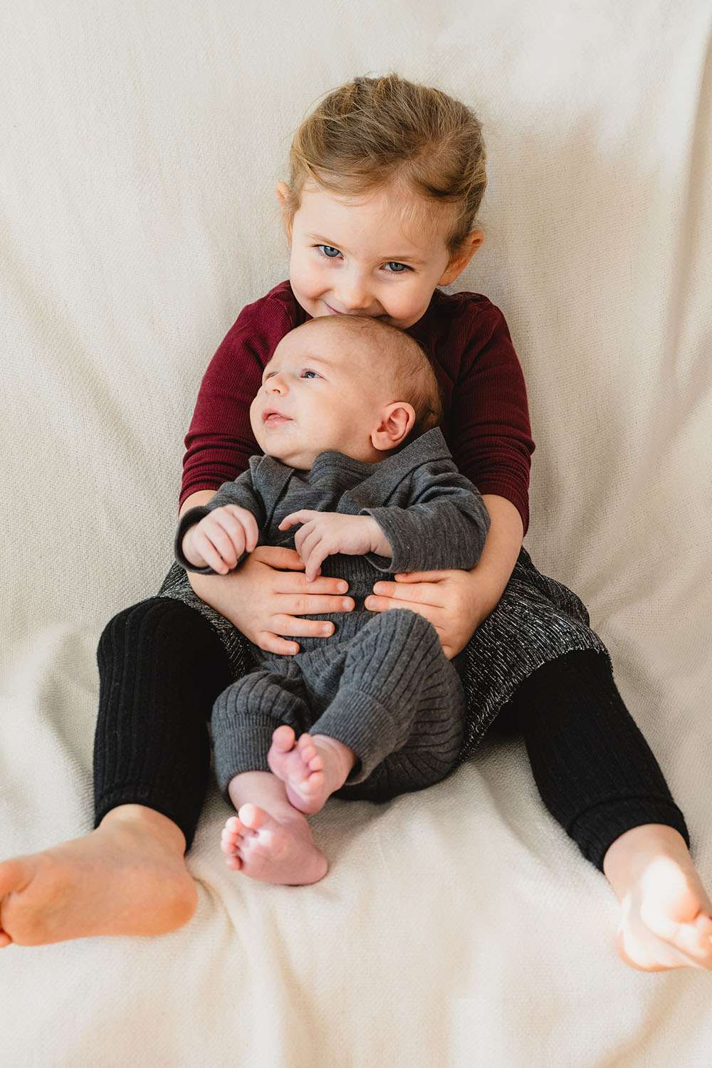 Kleines Mädchen sitzt mit einem Newborn auf dem Boden
